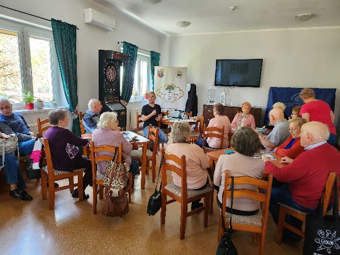 Fotografia przedstawia grupę seniorów, którzy siedzą i słuchają pogadanki na temat bezpieczeństwa w zakresie ochrony danych osobowych wygłoszonej przez przedstawiciela Stowarzyszenia Fidei Defensor.